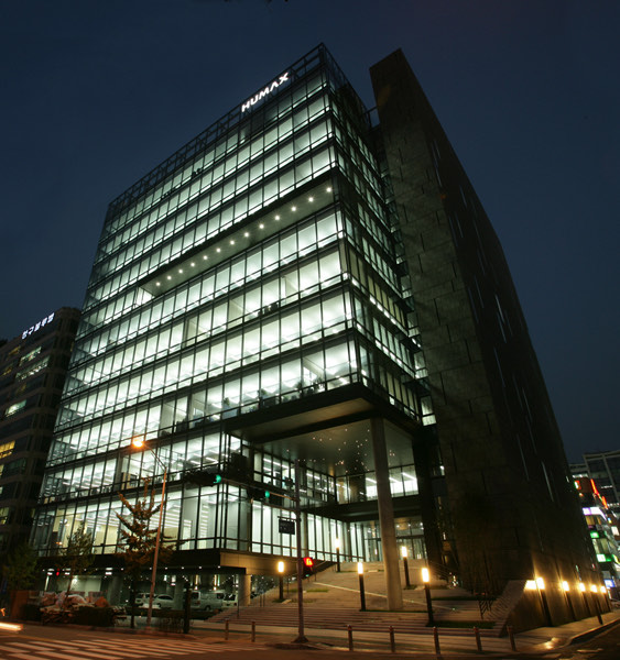 The Humax headquarters, a glass-fronted office building lit at dusk with the HUMAX sign on top