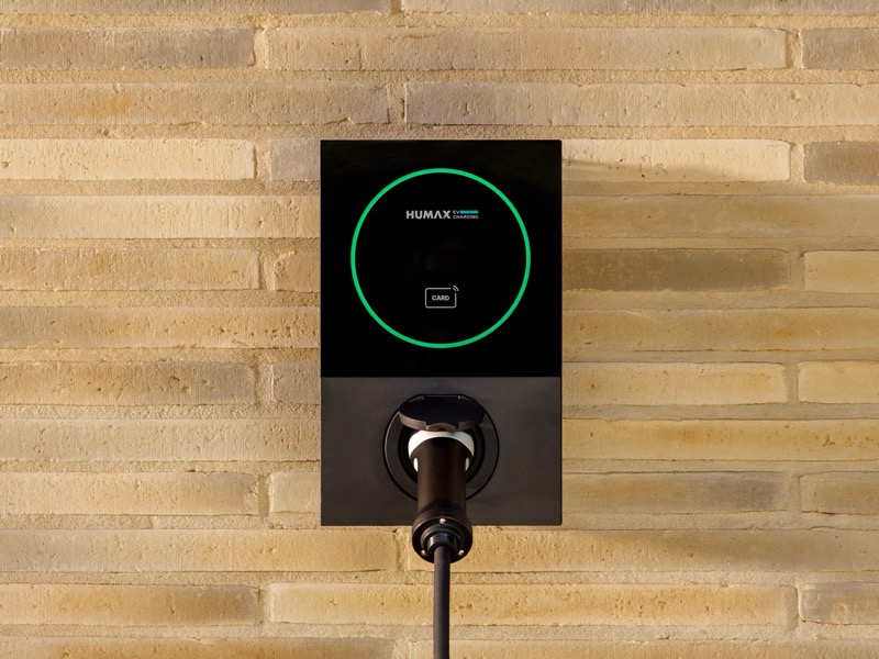 The Humax MX7 home EV charger mounted on a brick wall, its status ring glowing green